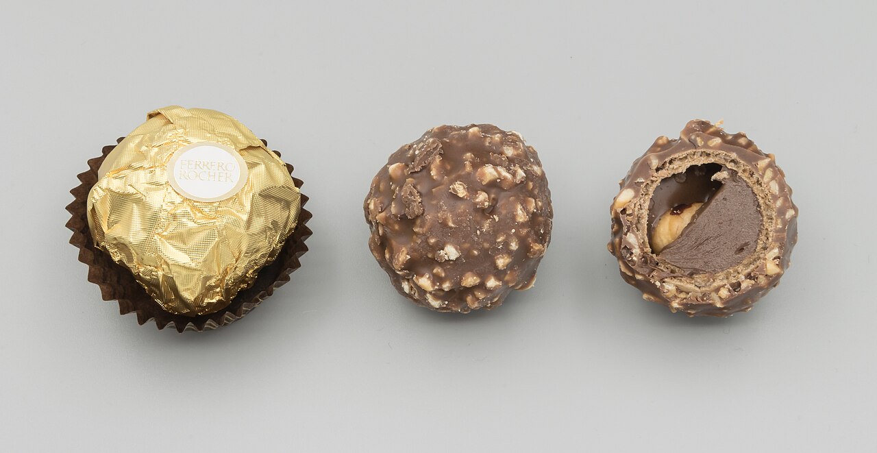 A Ferrero Rocher shown wrapped in its gold foil, unwrapped, and cut in half to show the hazelnut and filling